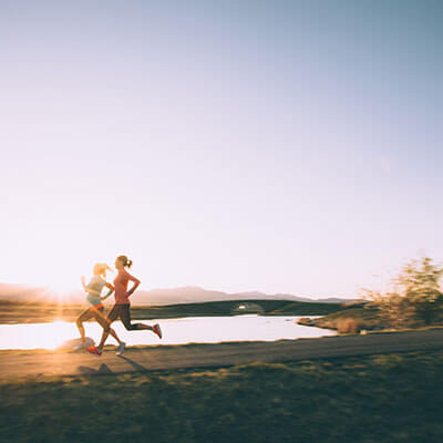 two women wearing performance cotton activewear run at sunrise by a lake