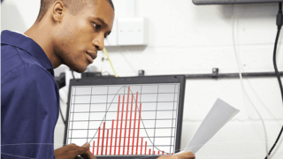 man reviewing paper with computer screen showing bar chart