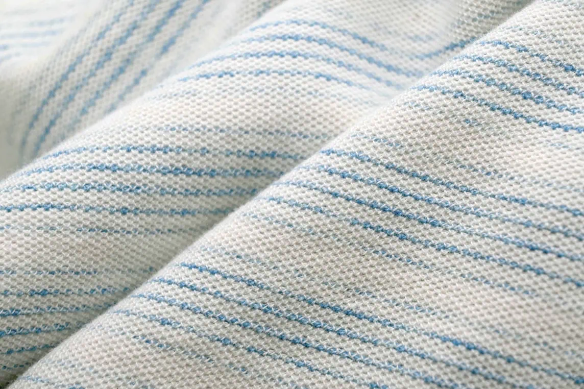 Close-up of 100% cotton double knit pique fabric with a natural cotton ground and stripes of blue mineral-dyed yarns.