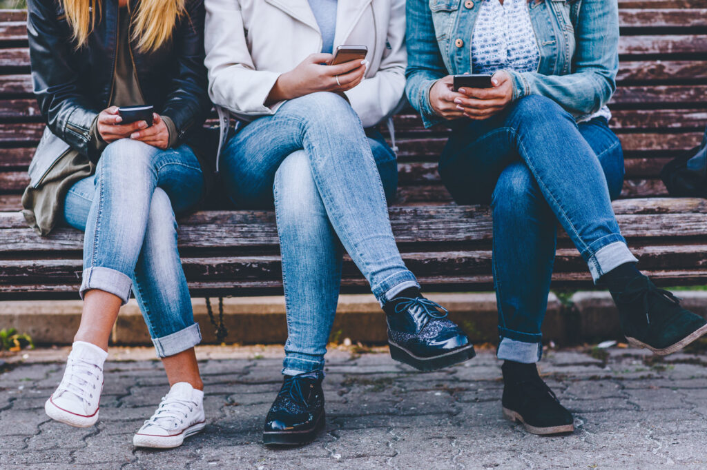 Three people wearing blue jeans while sitting together on a bench